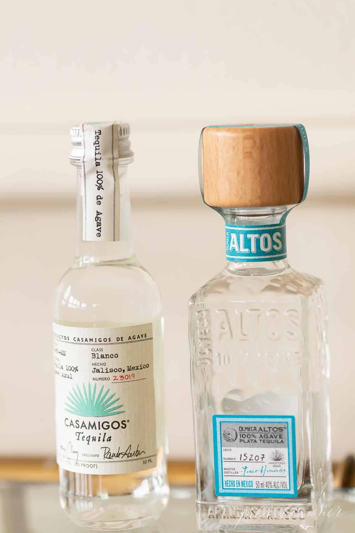 Two clear glass bottles of tequila for margaritas, on a glass bar cart.