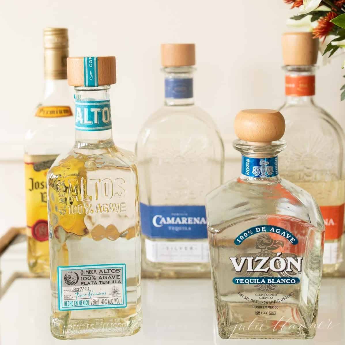 Five bottles of tequila on a clear glass bar cart.