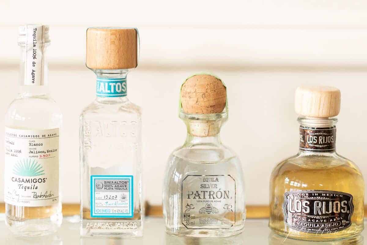 Four bottles of the best tequila for margaritas on a glass bar cart.