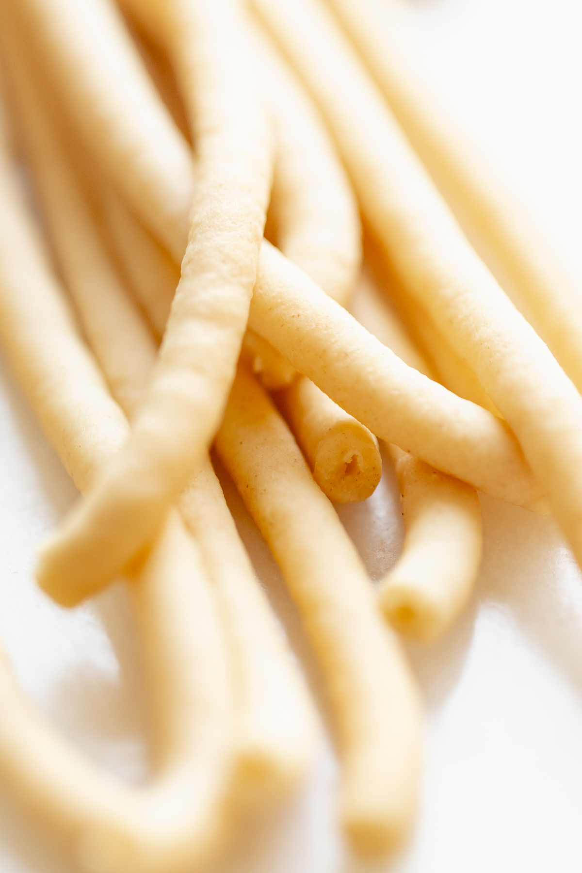 Close-up of bucatini noodles on a white background, highlighting their elongated shape and smooth texture.