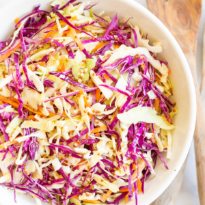 White salad bowl filled with colorful cabbage salad and wooden serving spoons.