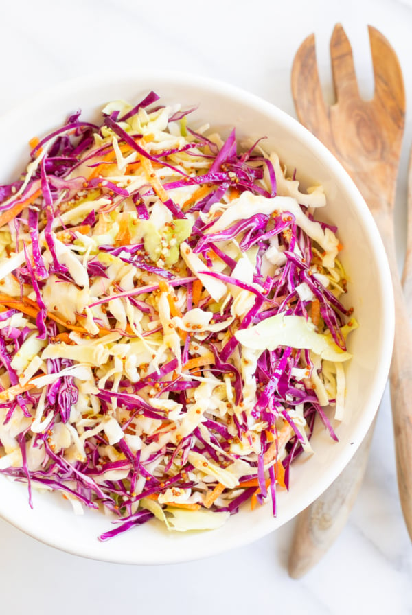 White salad bowl filled with colorful cabbage salad and wooden serving spoons.