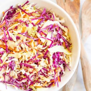 White salad bowl filled with colorful cabbage salad and wooden serving spoons.