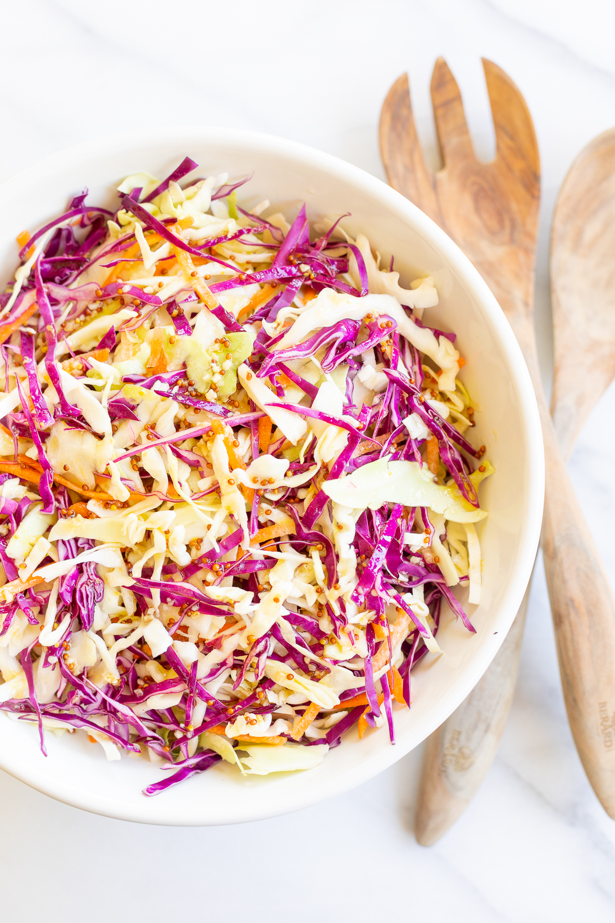 White salad bowl filled with colorful cabbage salad and wooden serving spoons.
