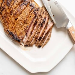 Sliced carne asada recipe on a white platter, knife to the side