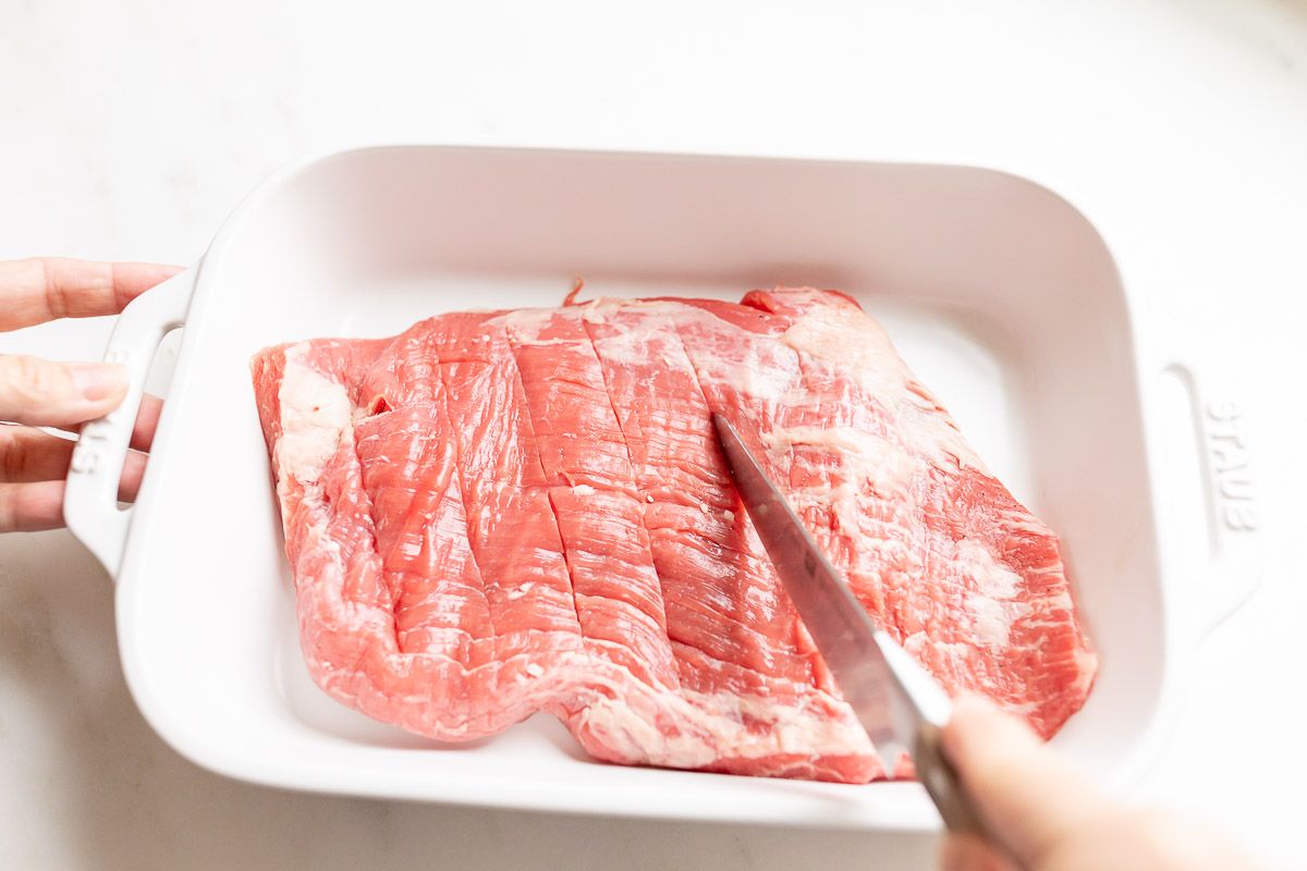A piece of flank steak in a white baking dish