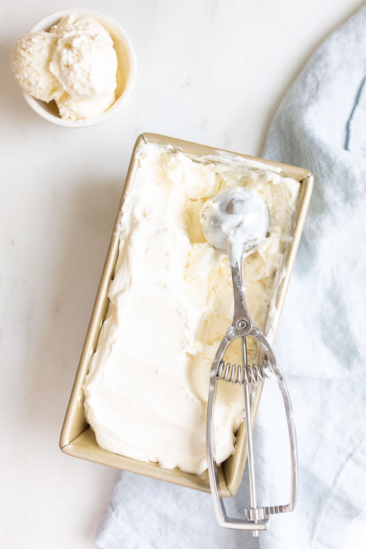 A gold metal loaf pan filled with a no churn ice cream recipe, with a scoop on top.