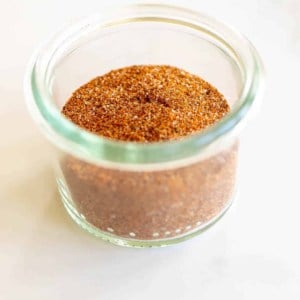 A marble surface with a clear glass jar full of homemade fajita seasoning mix.