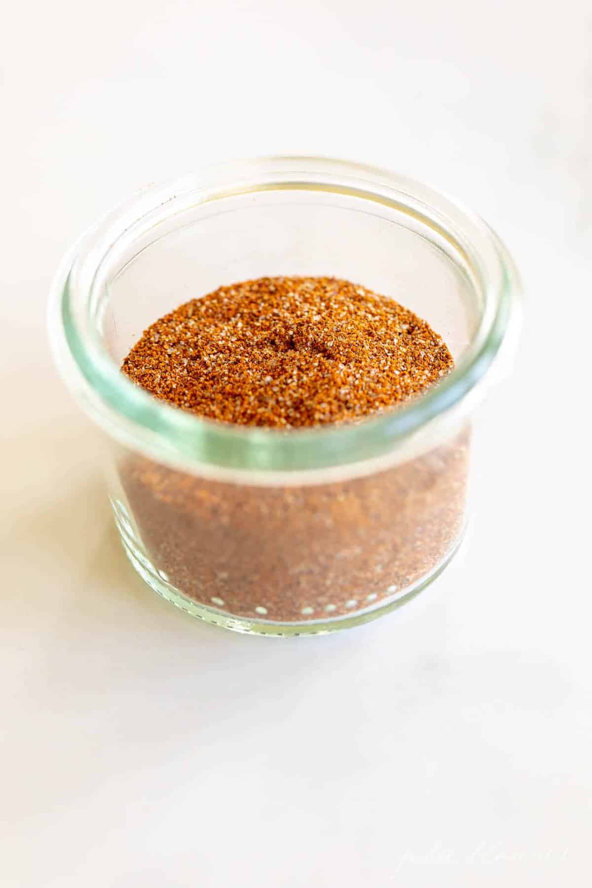 A marble surface with a clear glass jar full of homemade fajita seasoning mix.