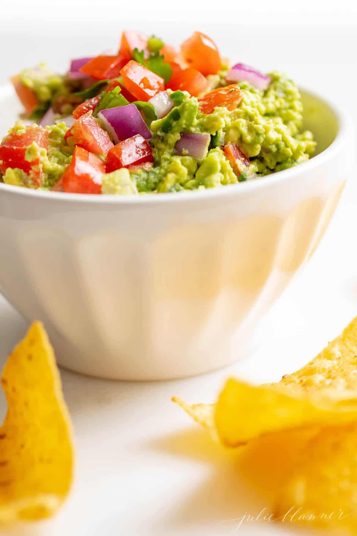 A white bowl full of homemade guacamole, chips to the side.