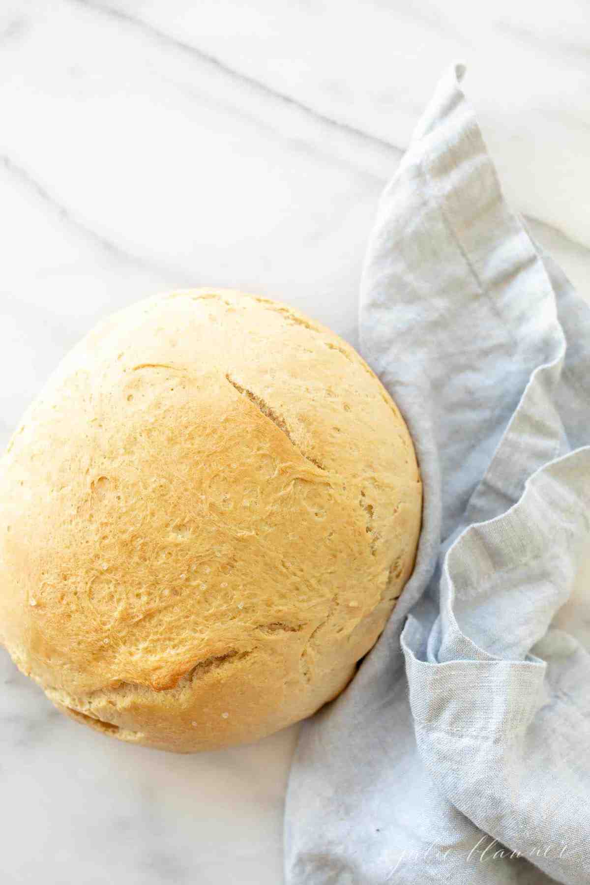 A loaf of homemade bread on a white surface, with a blue linen napkin on the side. 
