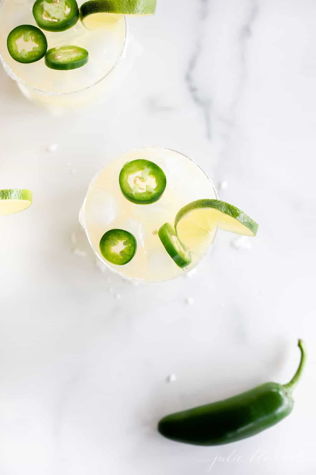 looking down into a clear glass full of spicy margarita topped with sliced jalapeno and lime.