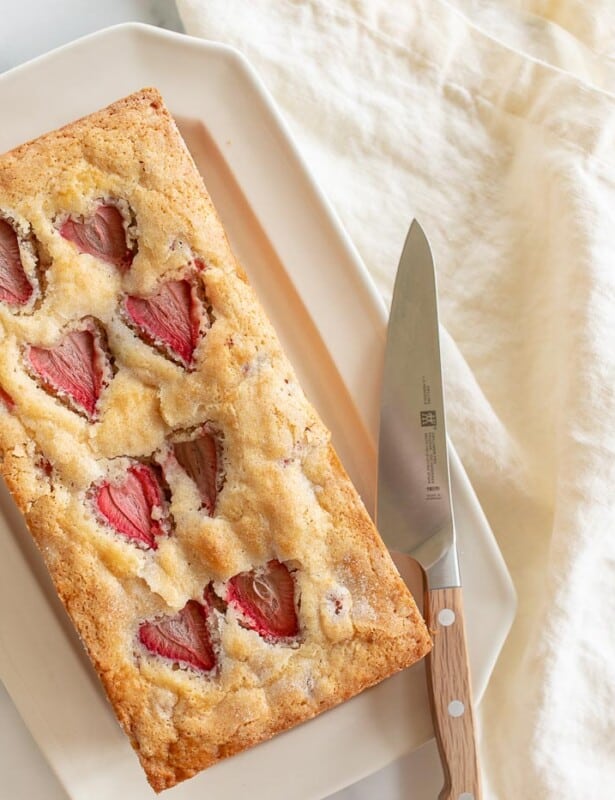 An ivory platter with a fresh loaf of strawberry bread, knife to the side.