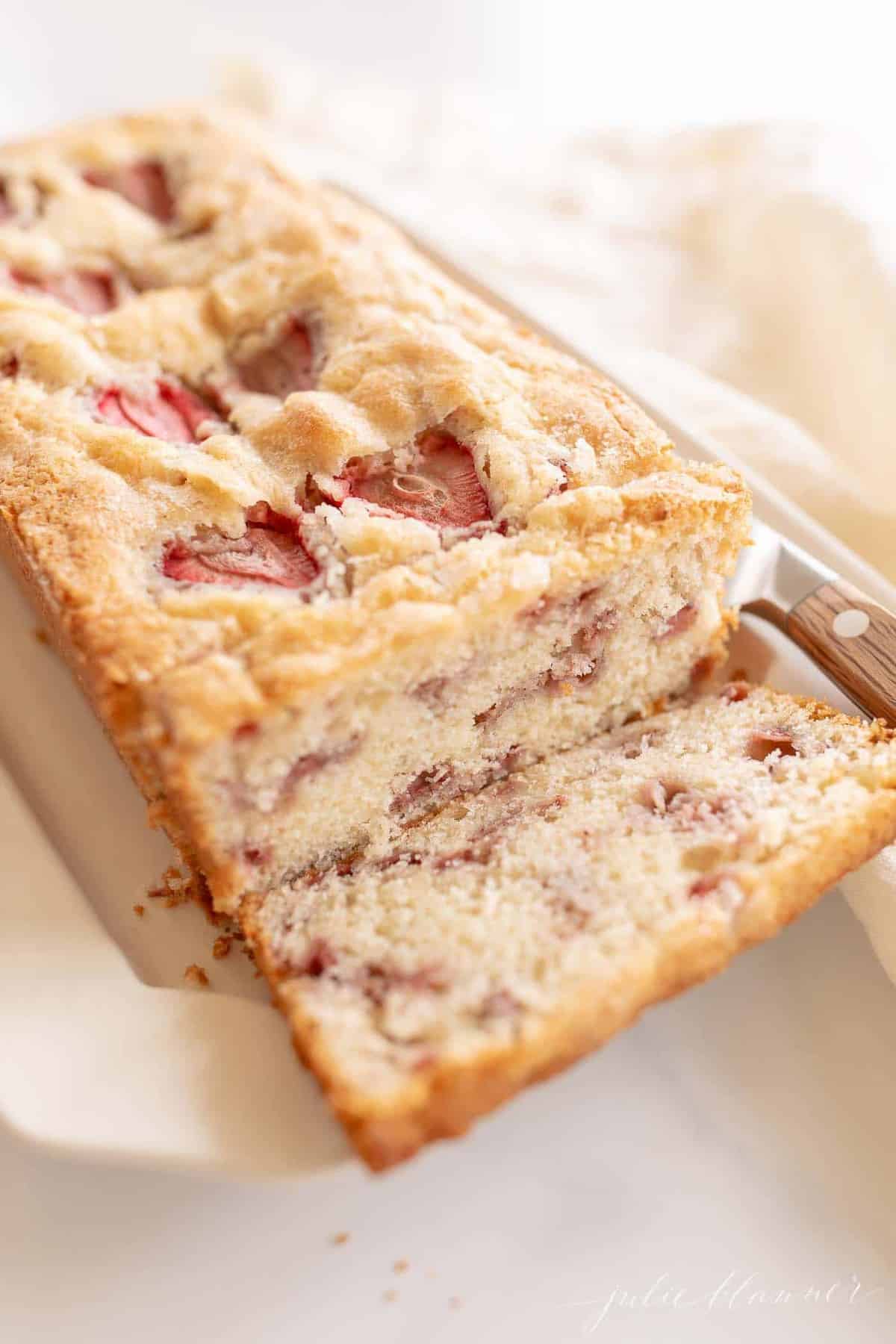 A loaf of strawberry bread, first slice cut off, knife to the side.