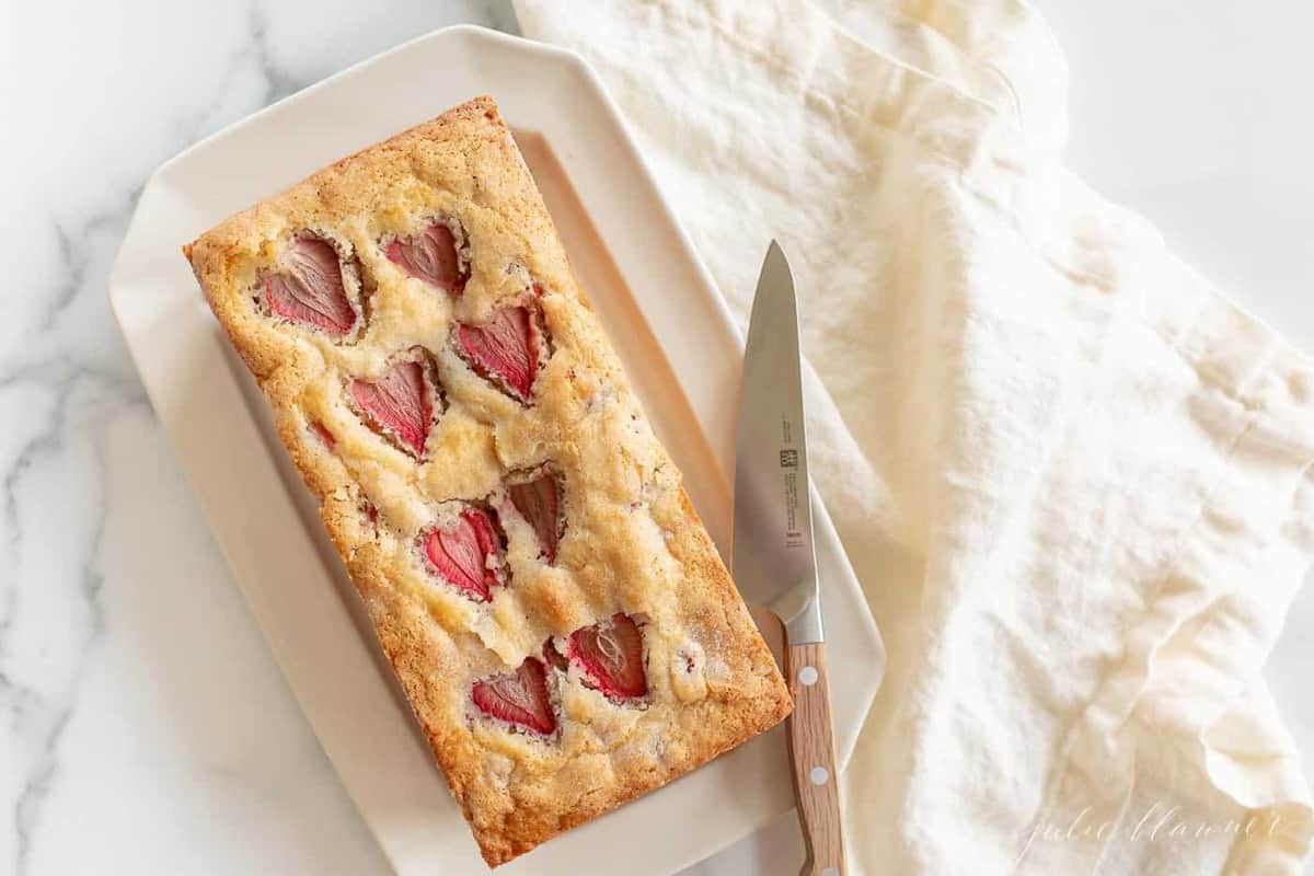 Strawberry bread on a white platter, a knife and linen napkin to the side. 