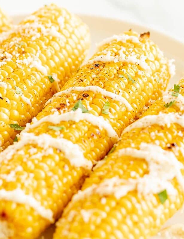 A white platter with an elote recipe of three mexican corn on the cobs, drizzled with cream sauce and cilantro.