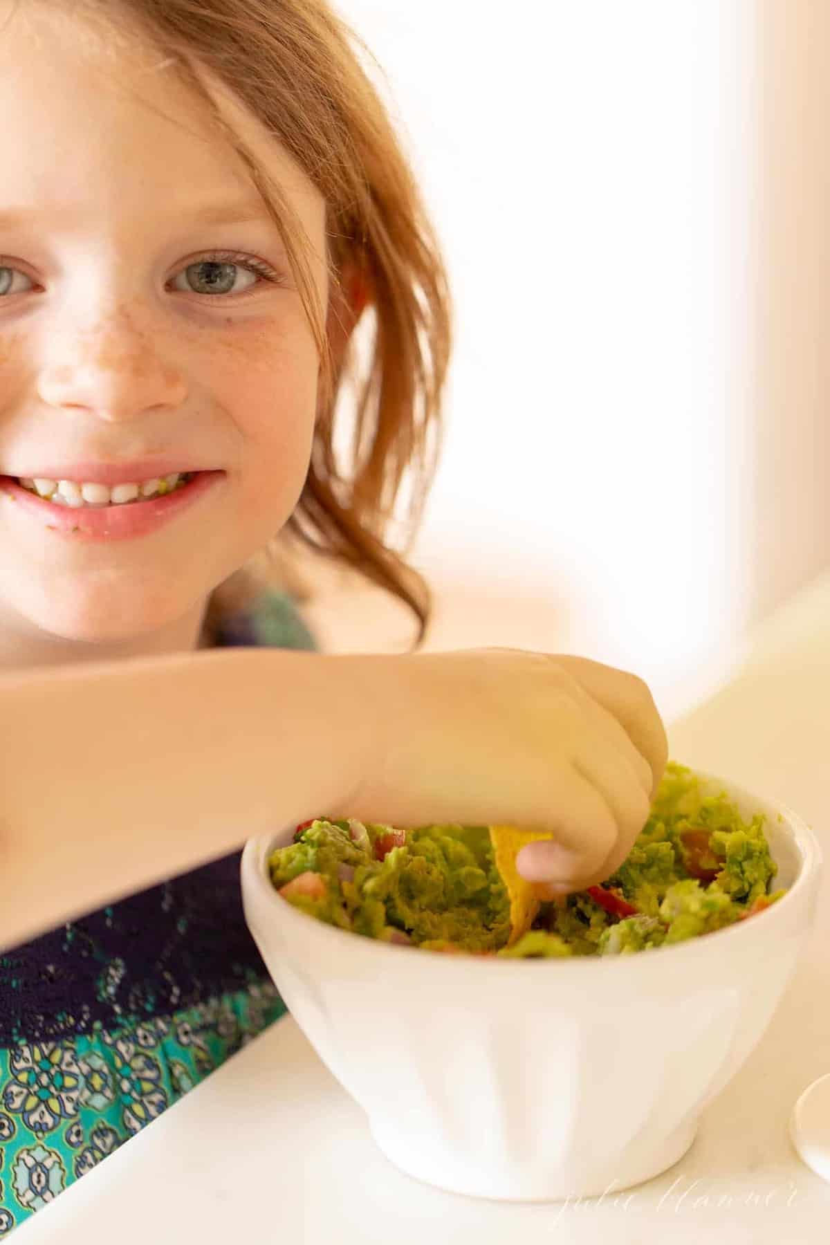 A little girl dipping into a bowl of homemade fresh guacamole.
