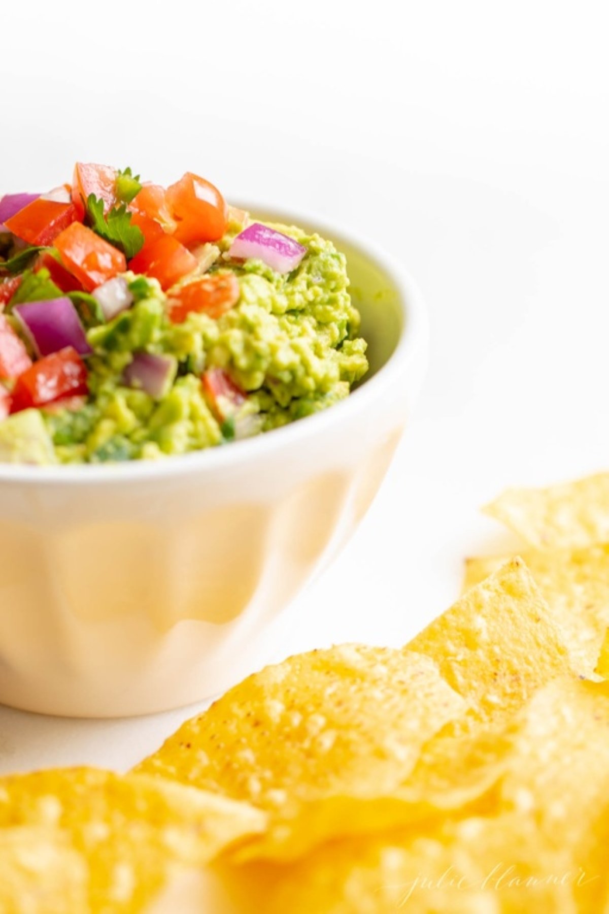 A white bowl full of fresh homemade guacamole., surrounded by tortilla chips.