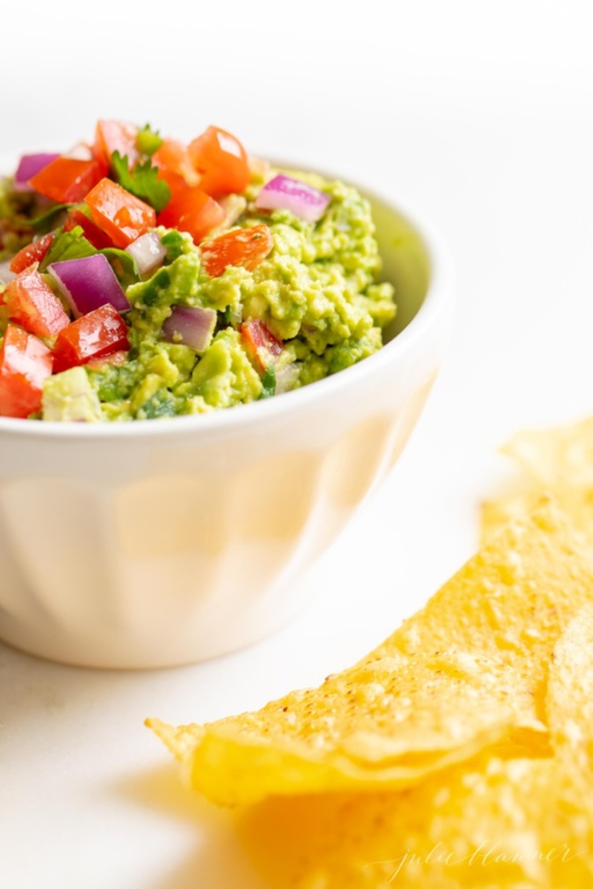 A white bowl full of fresh homemade guacamole., surrounded by tortilla chips. 