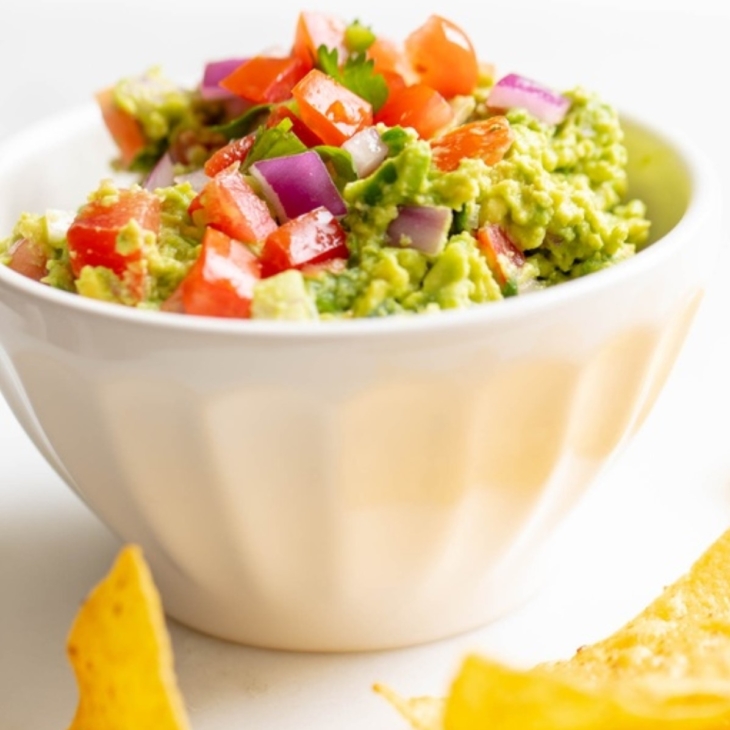 A white bowl full of fresh homemade guacamole., surrounded by tortilla chips.