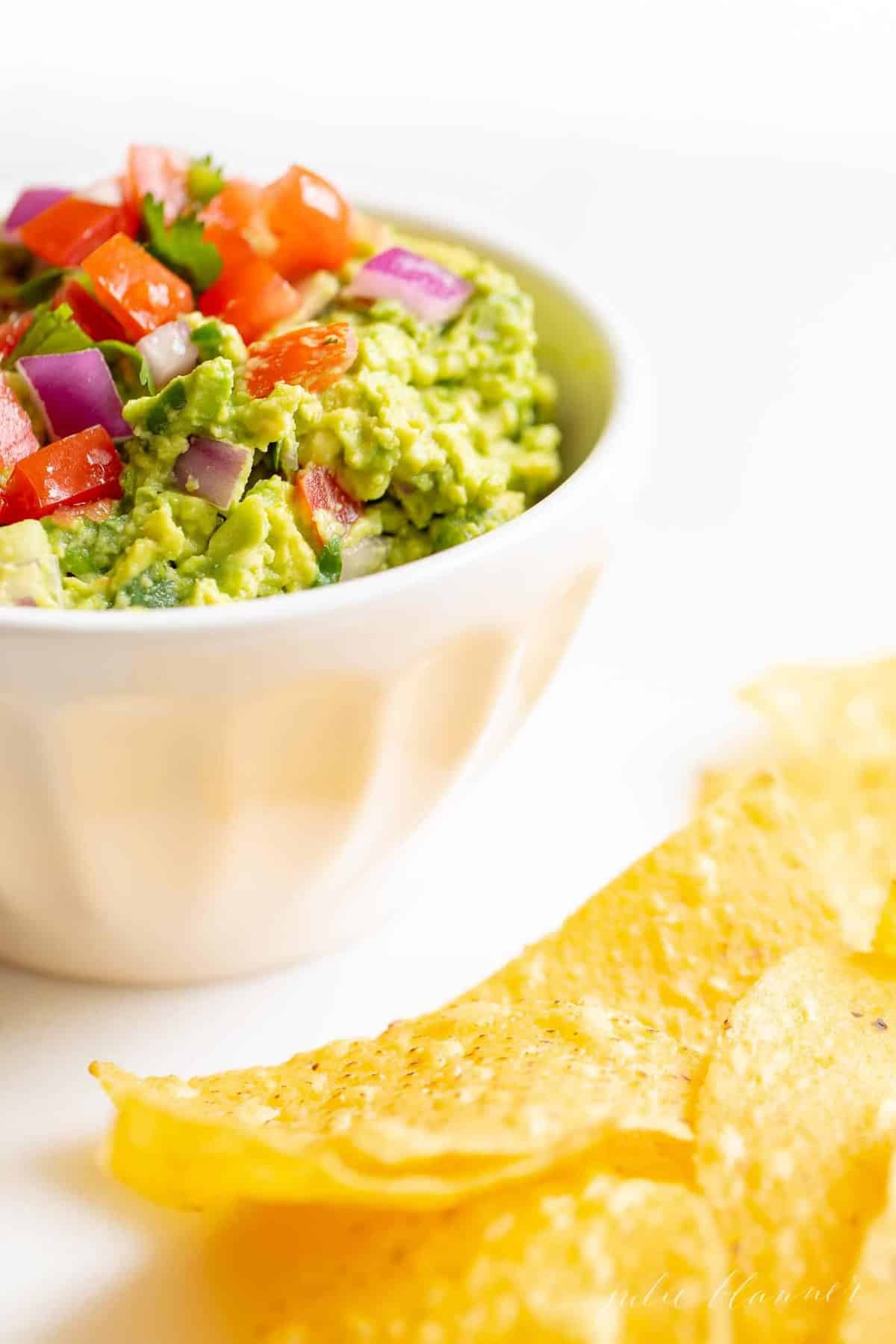 A white bowl full of homemade guacamole, chips to the side.