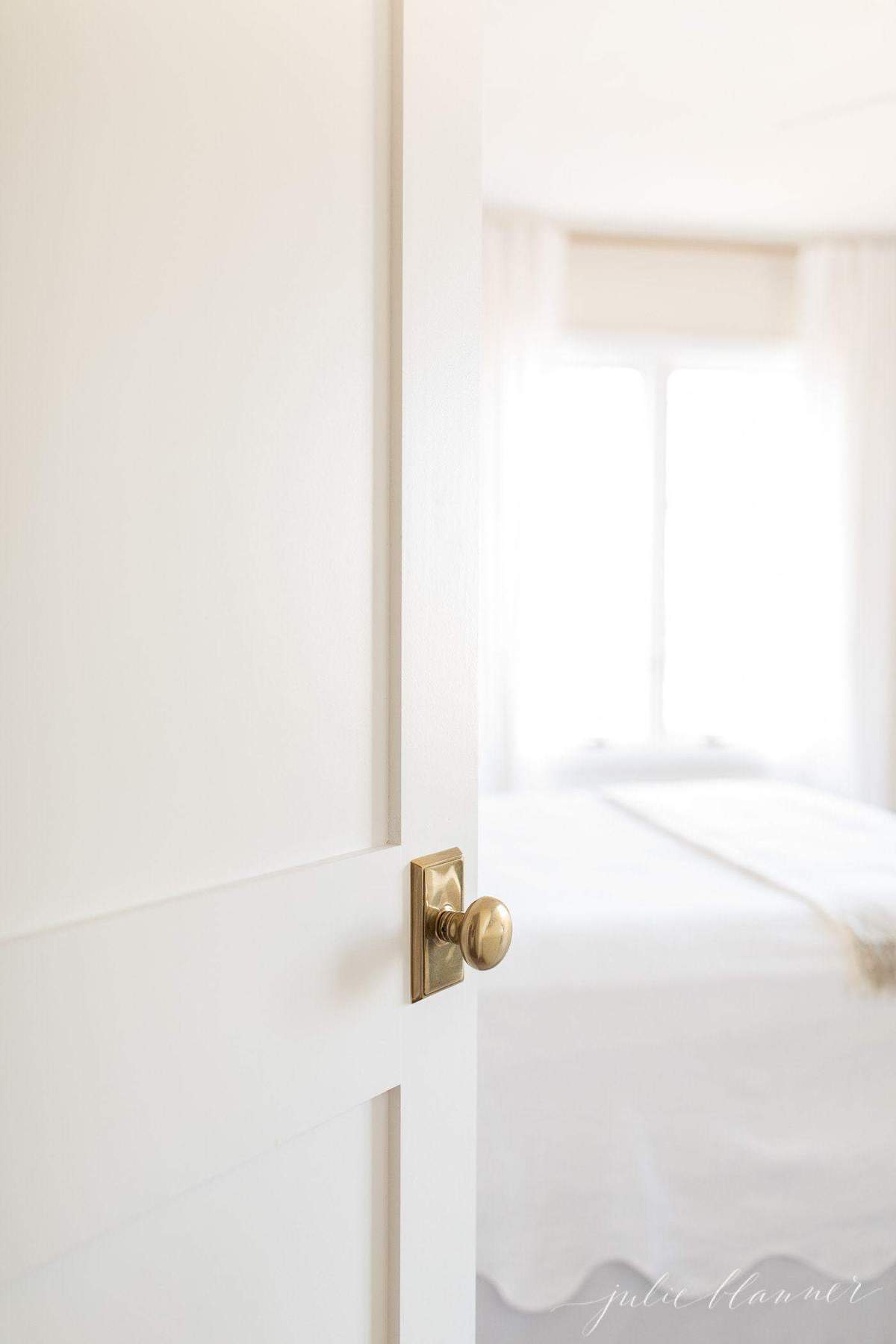 A new door with a brass doorknob peeking into a guest bedroom.