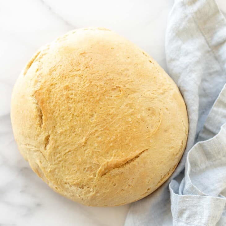 A marble surface with a round loaf of homemade bread, blue linen napkin to the side.