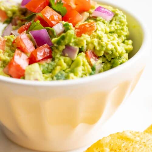 A white bowl full of homemade guacamole, chips to the side.