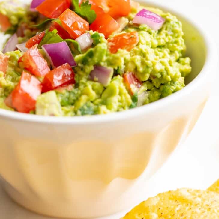 A white bowl full of homemade guacamole, chips to the side.