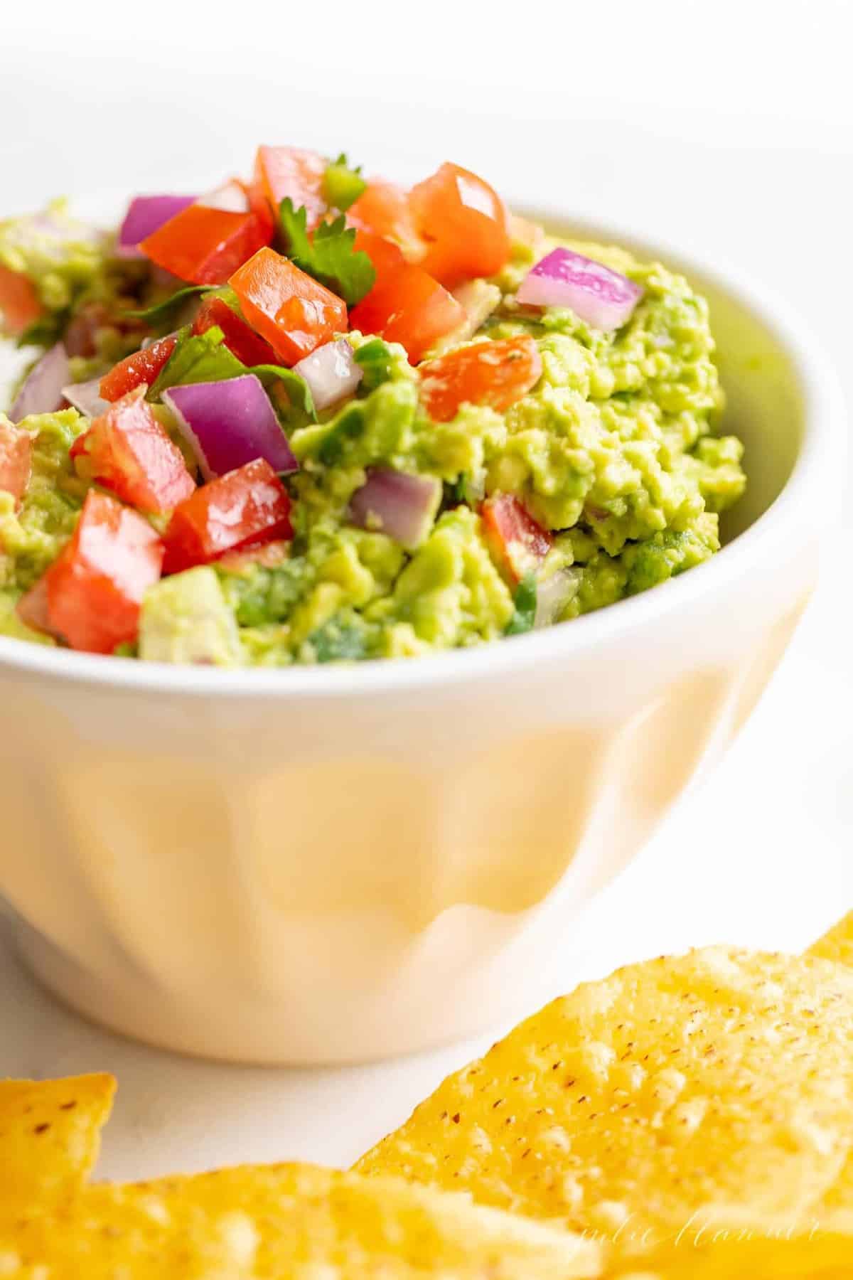 A white bowl full of homemade guacamole, chips to the side.