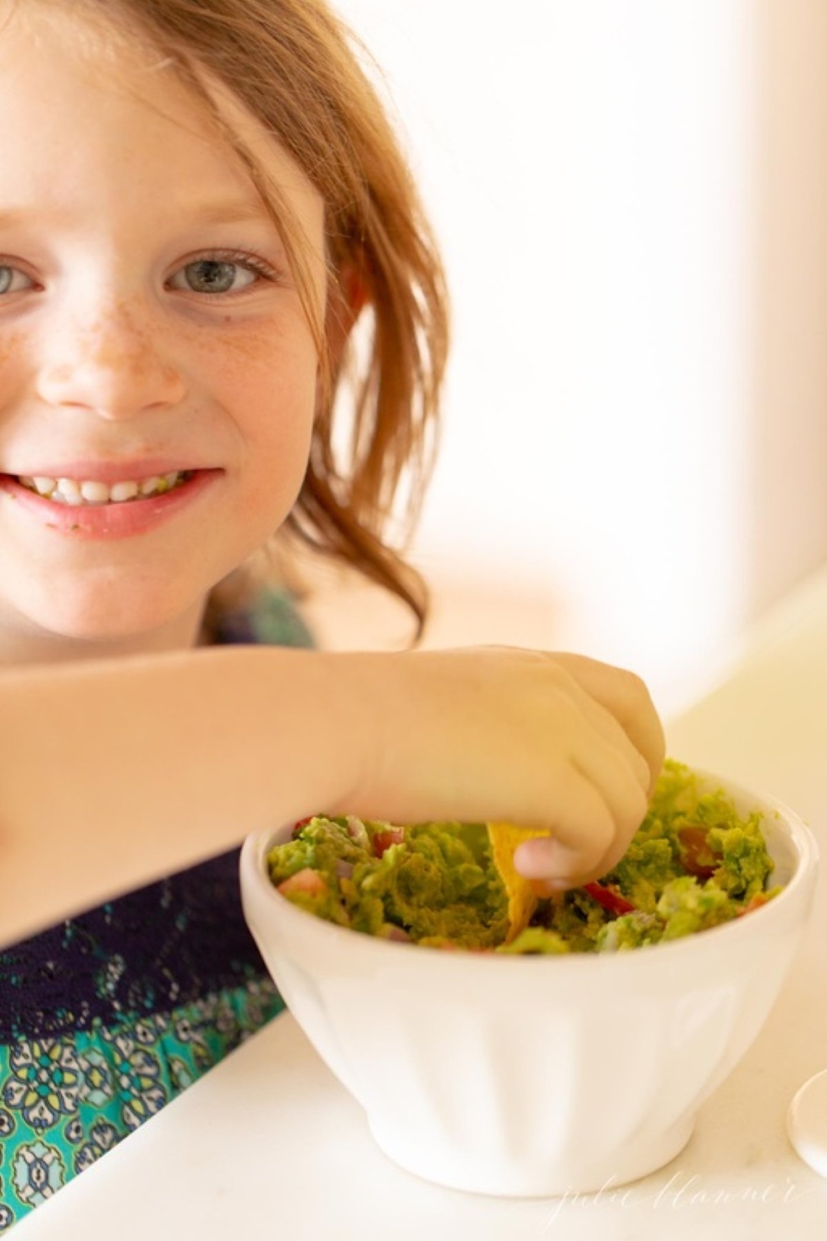 A little girl dipping a chip into a bowl of guacamole.