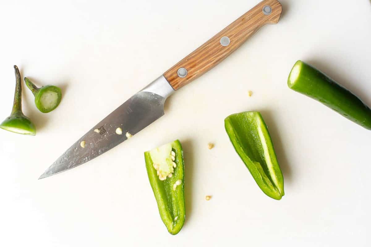 A marble surface with a knife and a split sliced jalapeno pepper.