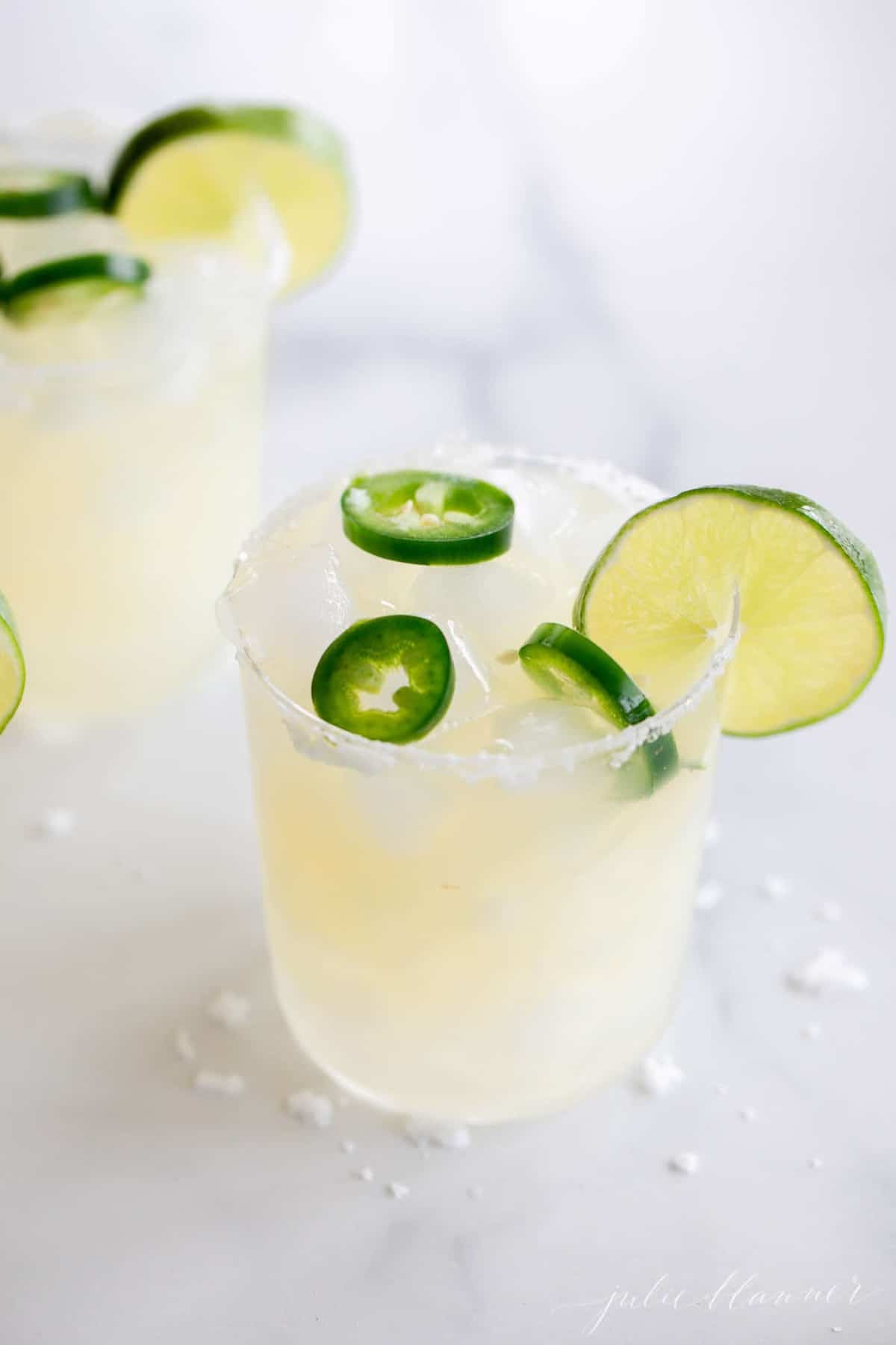 A marble surface with clear glasses full of spicy margarita recipe