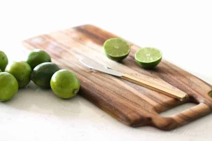 A wooden cutting board with sliced limes and a knife on top. 