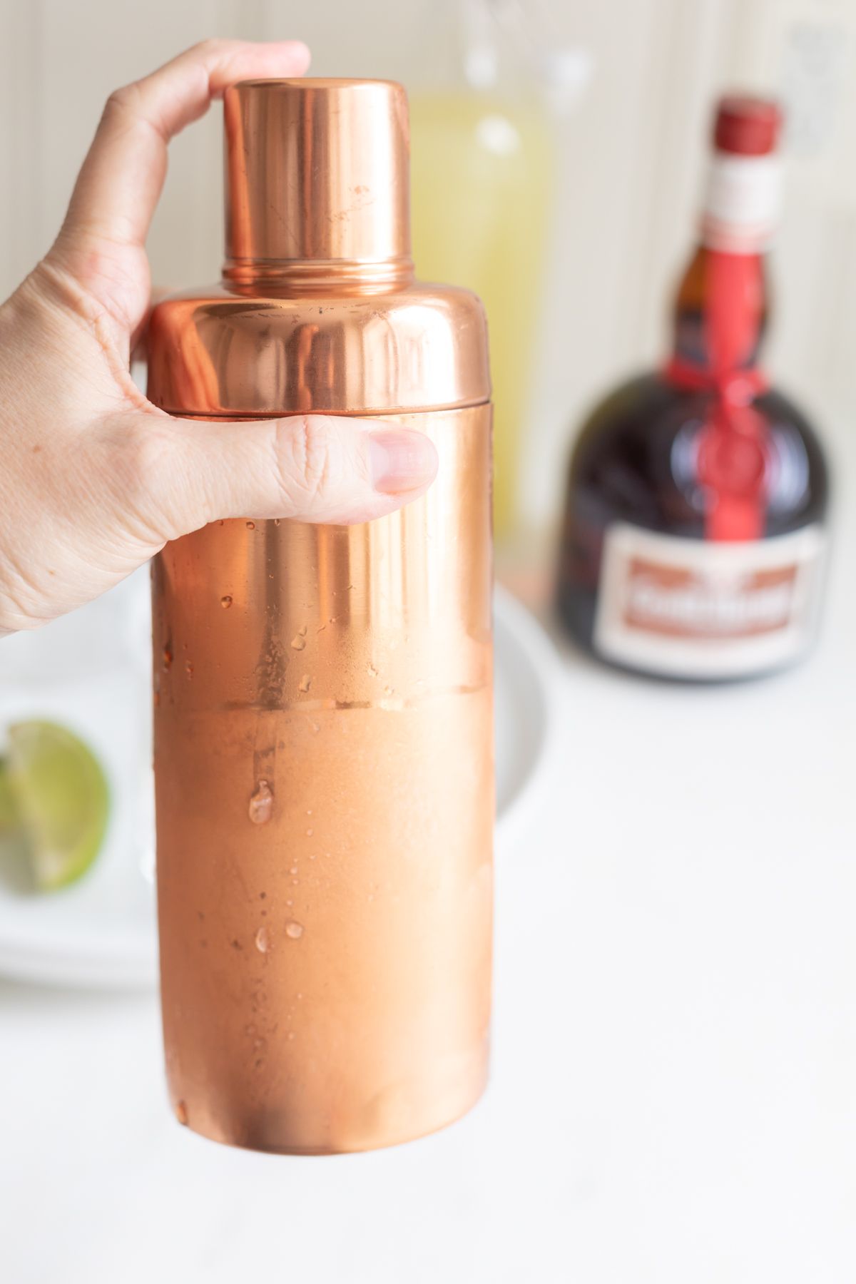 A copper shaker with a hand mixing up Cadillac margarita ingredients.