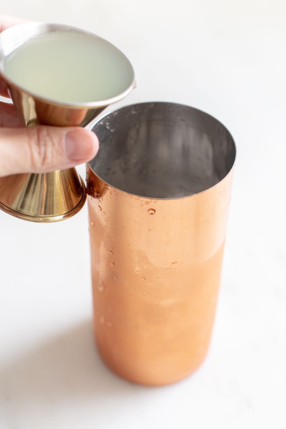 A copper shaker with a hand mixing up Cadillac margarita ingredients.