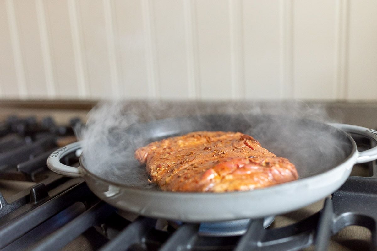 Carne asada recipe cooking in a cast iron pan on a stove top