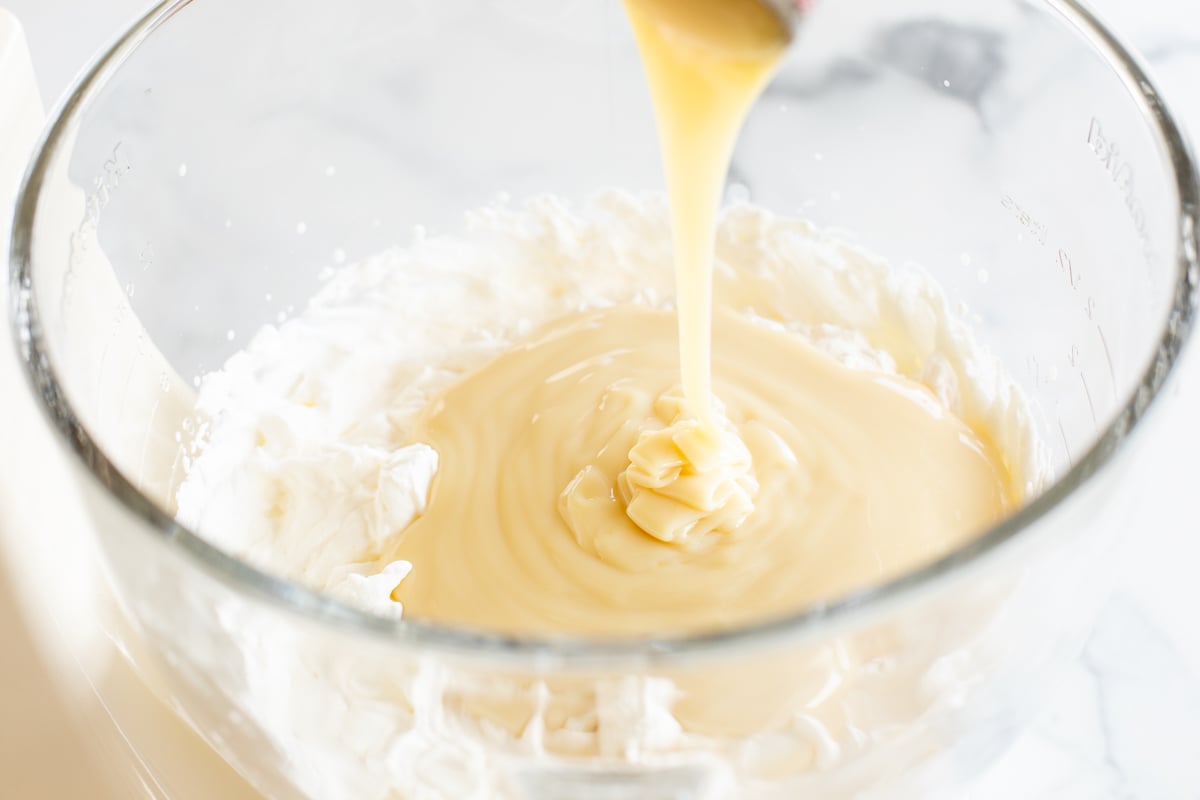 Condensed milk ice cream being whipped in the glass bowl of a stand mixer.