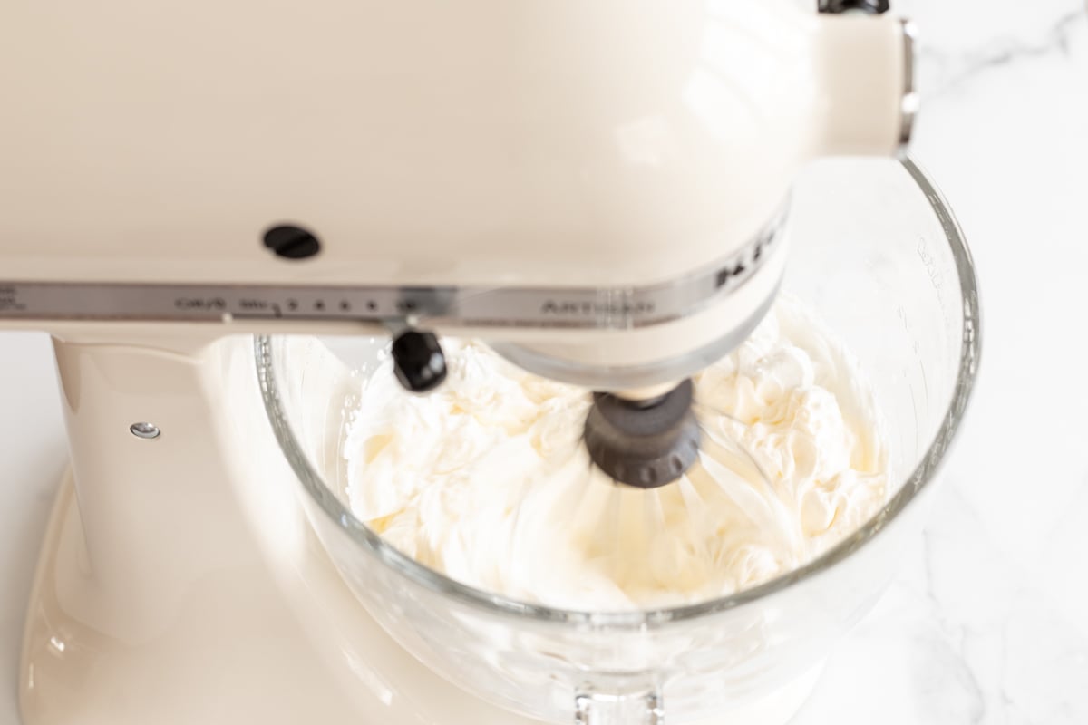 Condensed milk ice cream being whipped in the glass bowl of a stand mixer. 