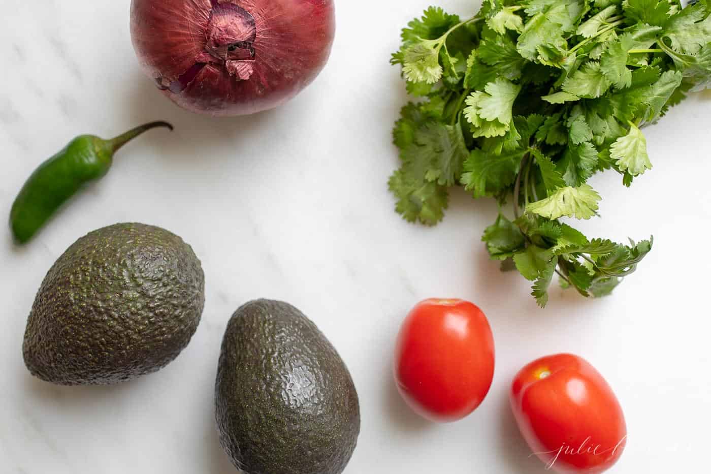 A white surface filled with the fresh ingredients for a guacamole recipe.