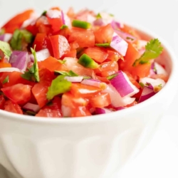 A white bowl full of fresh pico de gallo against a white background.