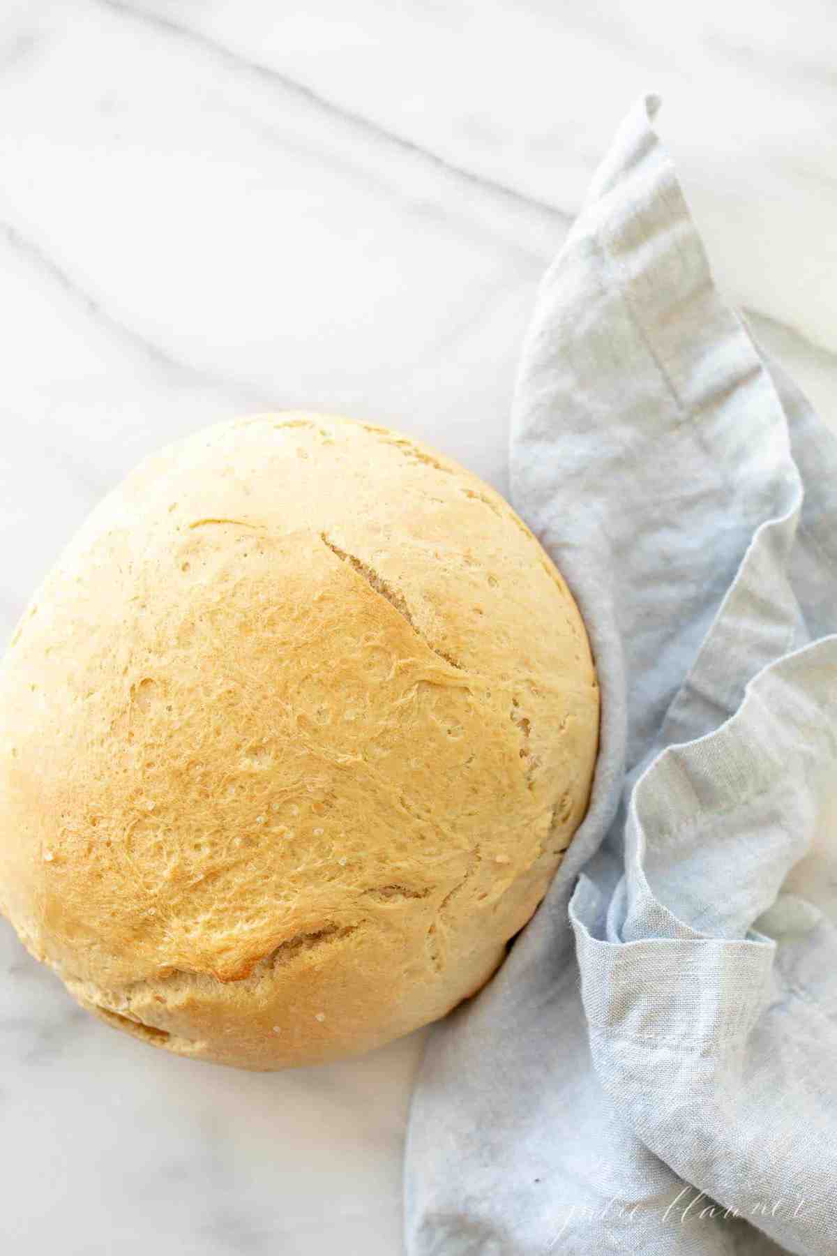 A round loaf of bread on a marble surface, blue linen napkin to the side.