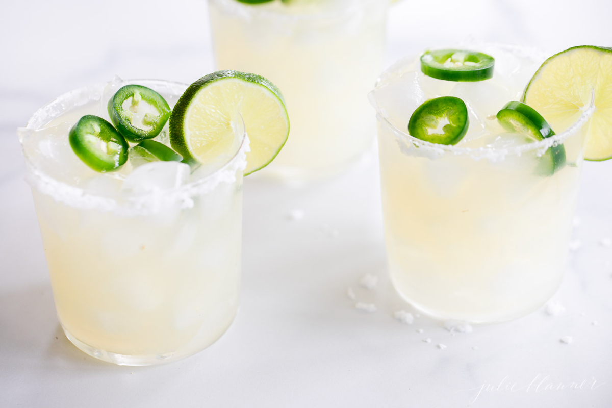 Three glasses of jalapeno margaritas with limes and jalapenos, created using a spicy margarita recipe.