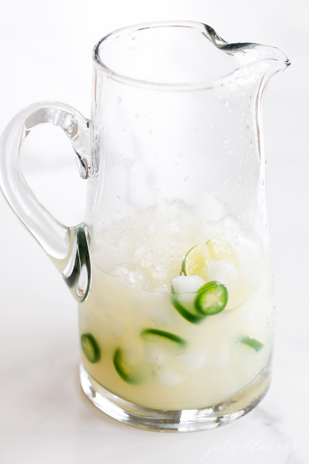 A pitcher filled with ice and jalapeños, perfect for making a spicy Jalapeño Margarita.