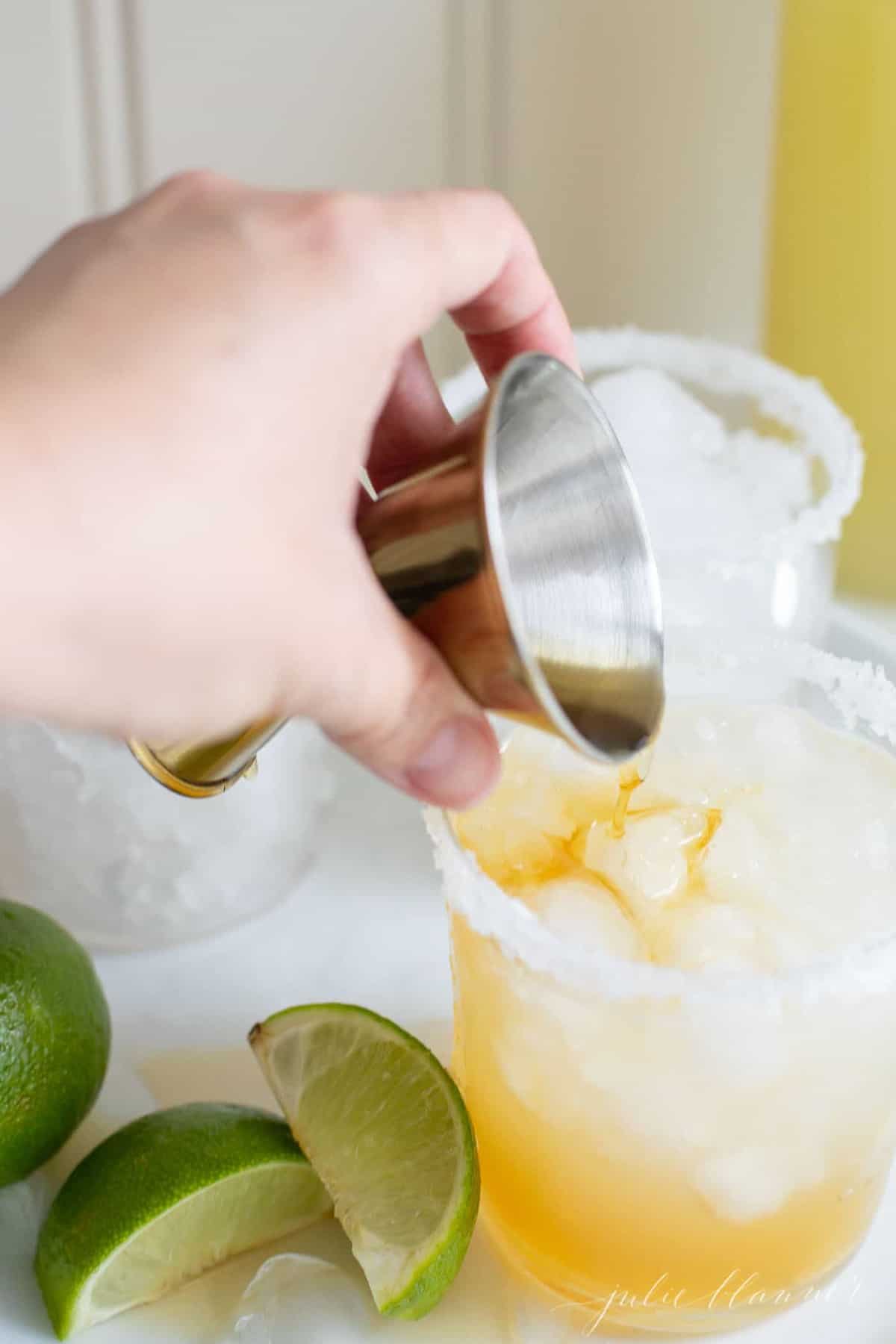 A hand pouring liquor into a glass of a made from scratch margarita.