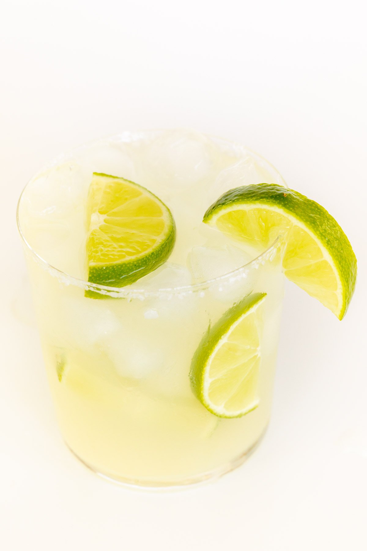 A clear glass with a homemade margarita recipe garnished with limes