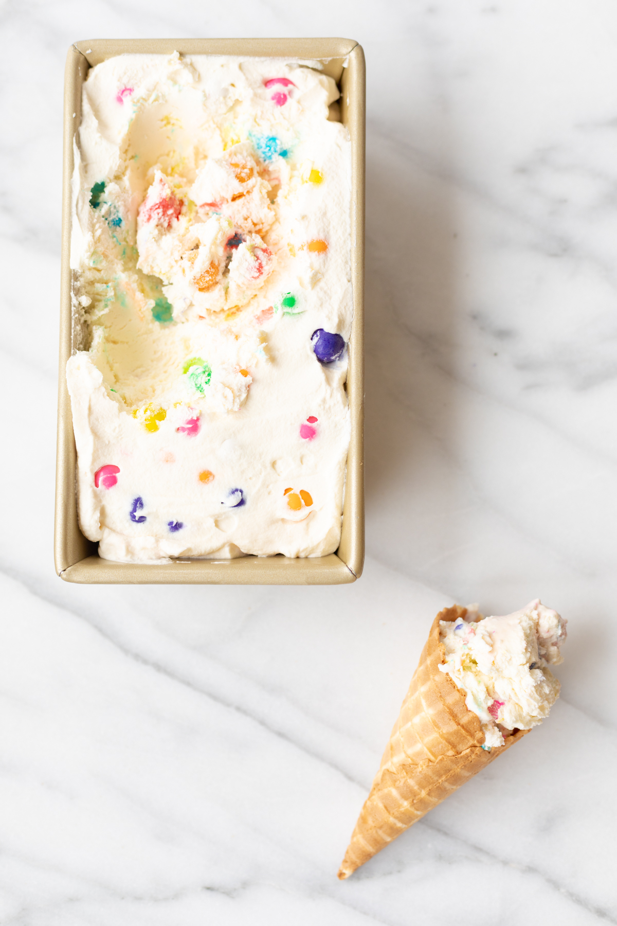 bubblegum no churn ice cream in a gold metal loaf pan, with an ice cream cone to the side. 