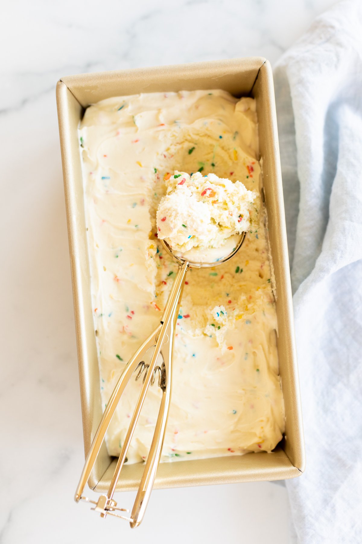 A gold metal loaf pan filled with a no churn ice cream recipe, with a scoop on top. 