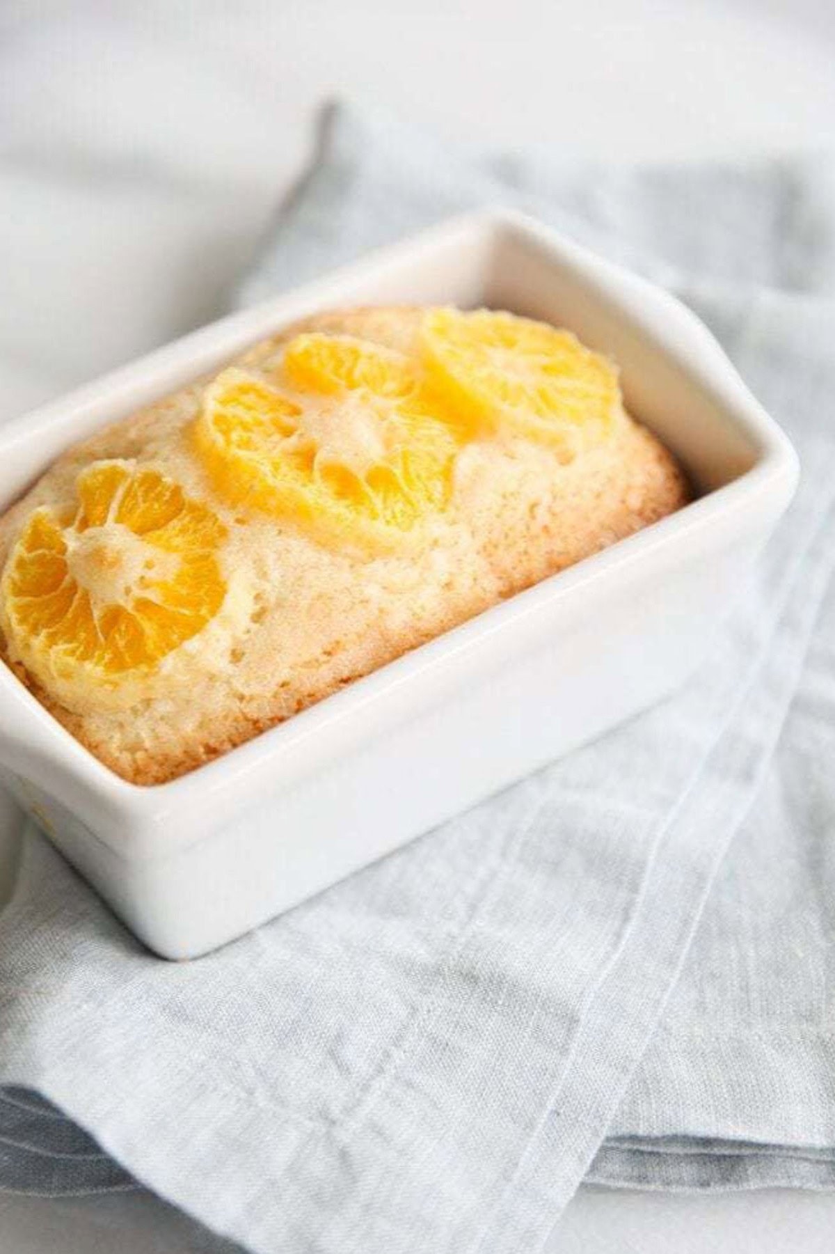 A rectangular loaf of quick orange bread topped with lemon slices in a white baking dish on a light gray cloth.