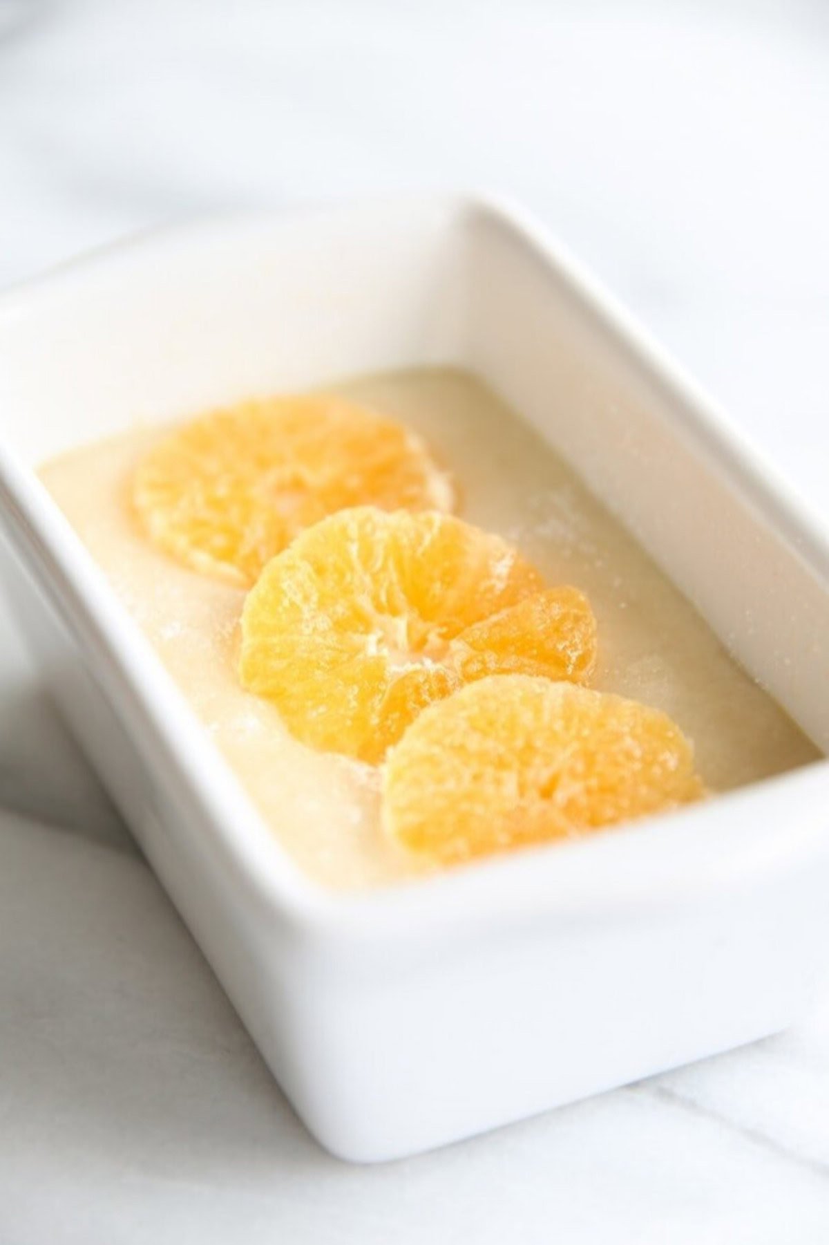 A small rectangular white dish contains a creamy dessert topped with four thin slices of orange, reminiscent of the zest in quick orange bread.